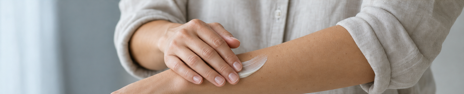 A hand applying moisturizer to a forearm, framed by linen sleeves.